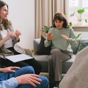 Women in casual clothes sitting on sofa and speaking during group psychotherapy session in cozy office